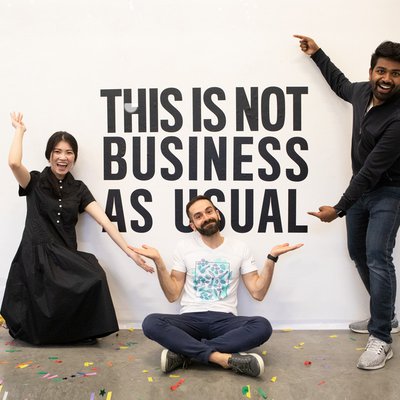 Three students pose for a photo in front of a wall that says, "This is not business as usual."