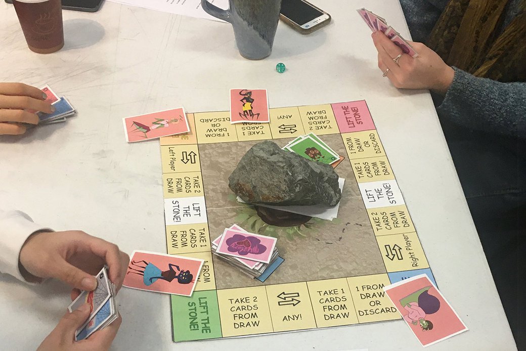 Three people play a board game in a classroom.