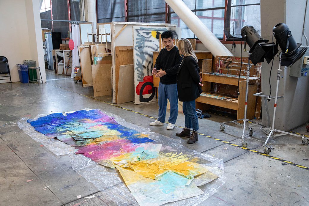 A student looks at a large-scale painting on the floor with Professor Linda Geary.