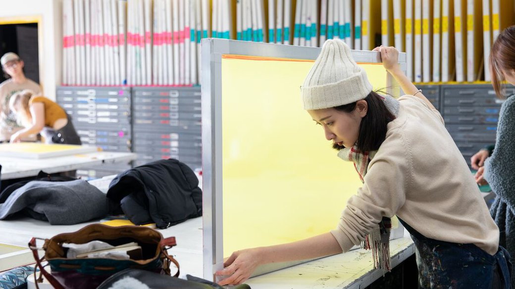 A student tapes off the edge of a screen in the printmedia studio.