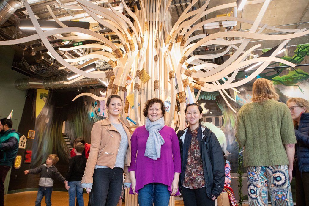 People posing in front of a large tree-shaped construction with many branches.