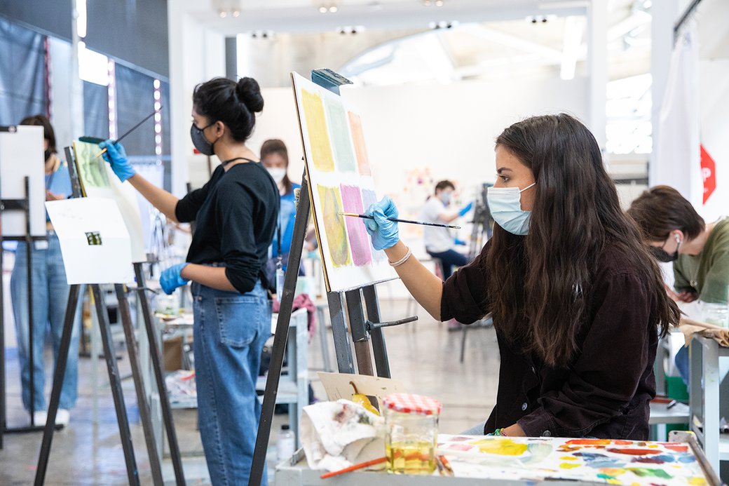 Two students paint at easels in the painting and drawing studio.