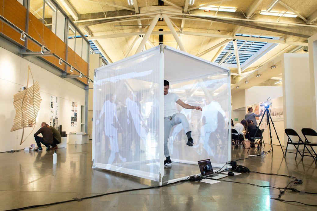 A student dances inside of a white cube covered in projections.