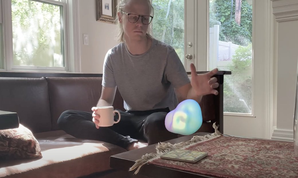 A student sits on a sofa with a neon-colored orb floating in front of them.
