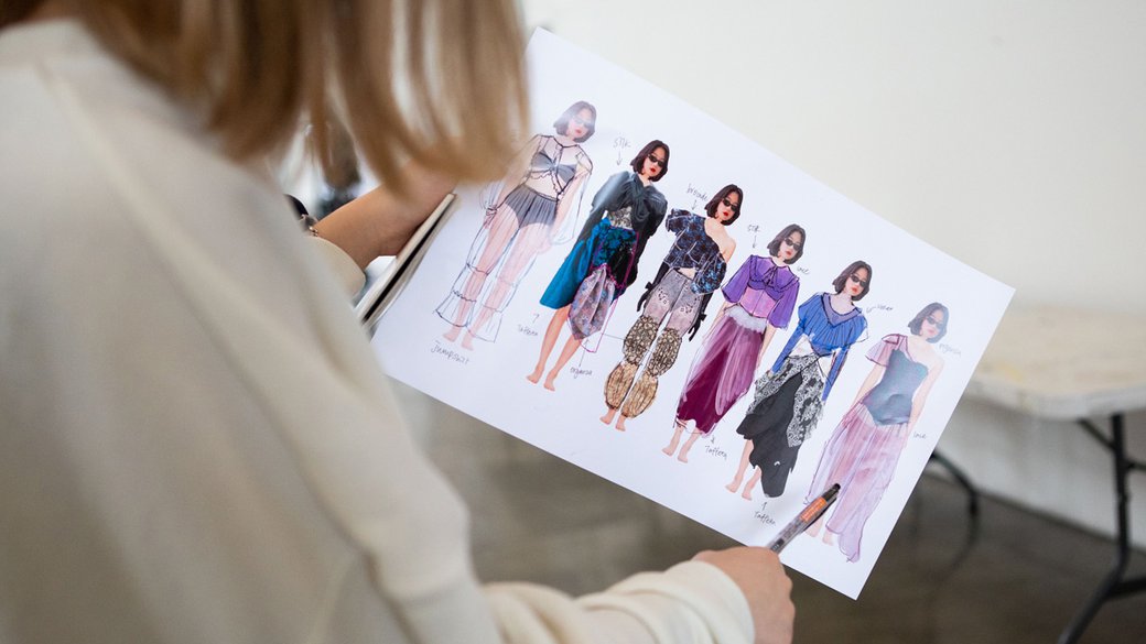 A student holds a drawing of multiple fashion garments.