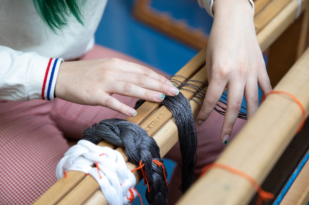 Close-up photograph of a student's hands as they work on a floor loom in the Weaving Studio.