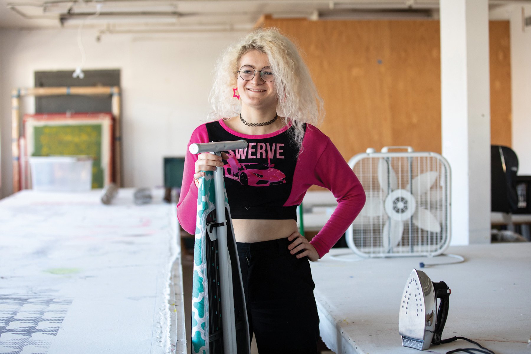 A student, Anna Nunes (BFA Textiles 2020), stands with an ironing board.