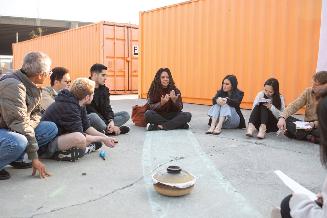 A group of students and a professor sit in a circle on the San Francisco campus’s Backlot.