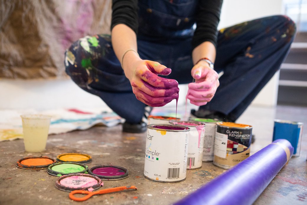 A painting student using her hands to apply pigment to canvas