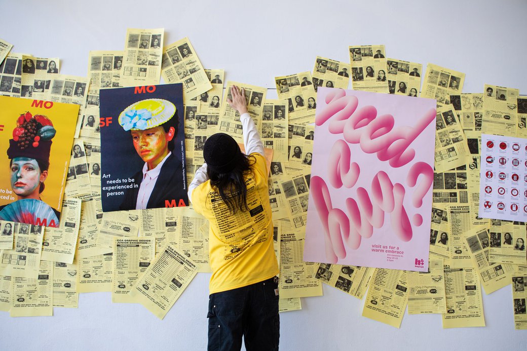 A student pins up graphic posters on a white wall in the Nave.