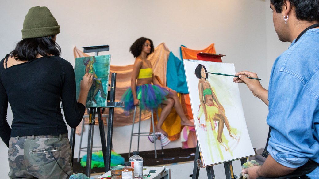 Students paint a model who is posing on a platform.