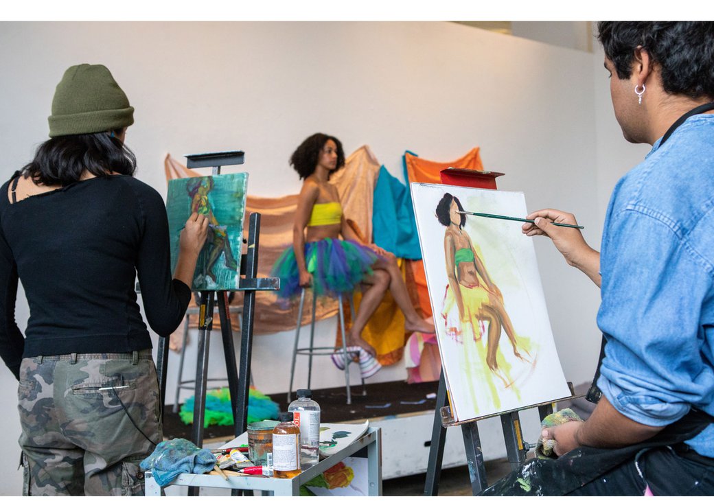 Students paint a model who is posing on a platform.