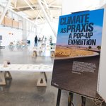 The image features a poster for CCA's Gensler Center opening, titled "Climate as a Praxis, a Pop-Up Exhibition," with the exhibition slightly blurred in the background.