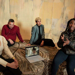 This photo is of five artists, four sitting around a museum's common area and one on a laptop Zoom call. They are discussing their projects.