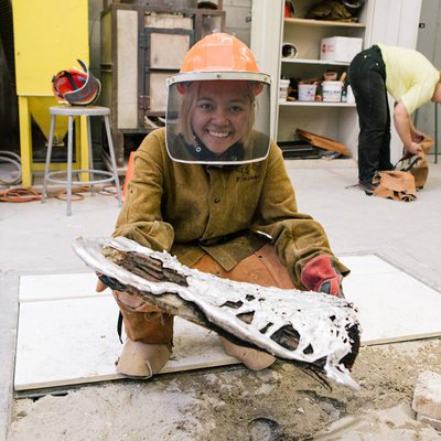 Sculpture student holds up their aluminum sculpture in the foundry.