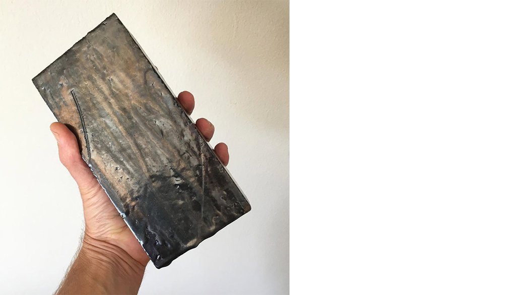 A hand holding a handmade ceramic brick.