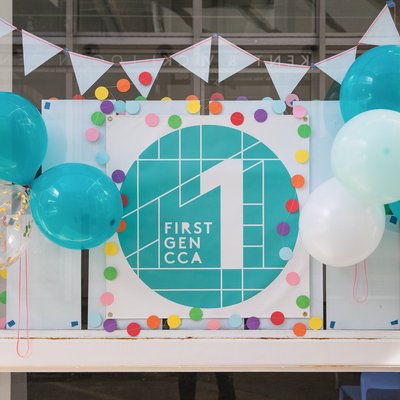 A photo of a sign which reads “First Gen CCA 1” surrounded by confetti and teal balloons.