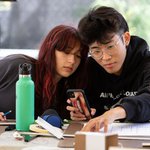 Two students use a straight edge over small cardboard maquettes.
