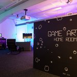 A room with a video game set up in the background and a wall with the text “Game Arts Home Room” in the foreground.