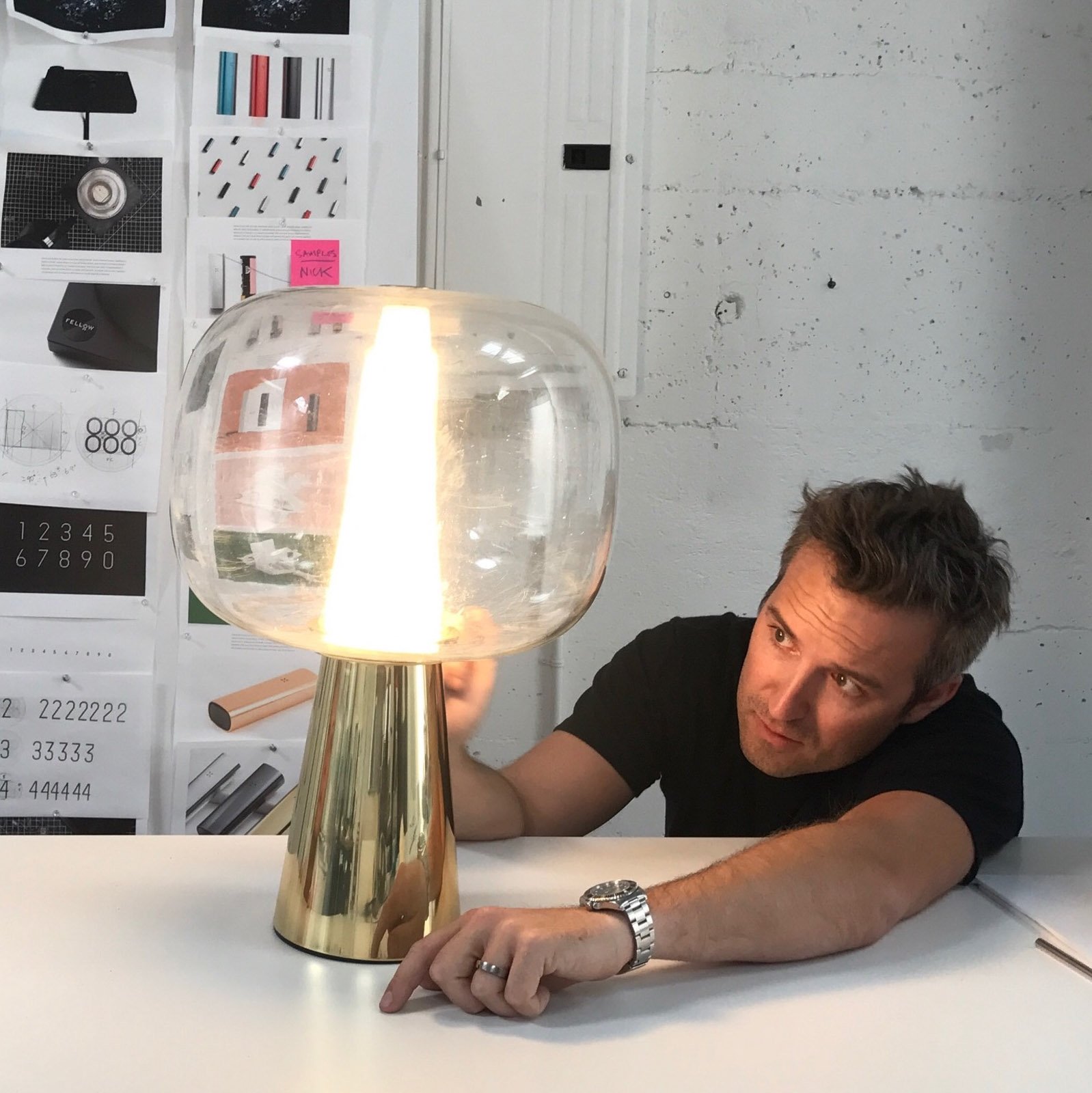 A man in a black t-shirt closely inspects a modernist illuminated lamp made of metal and glass.