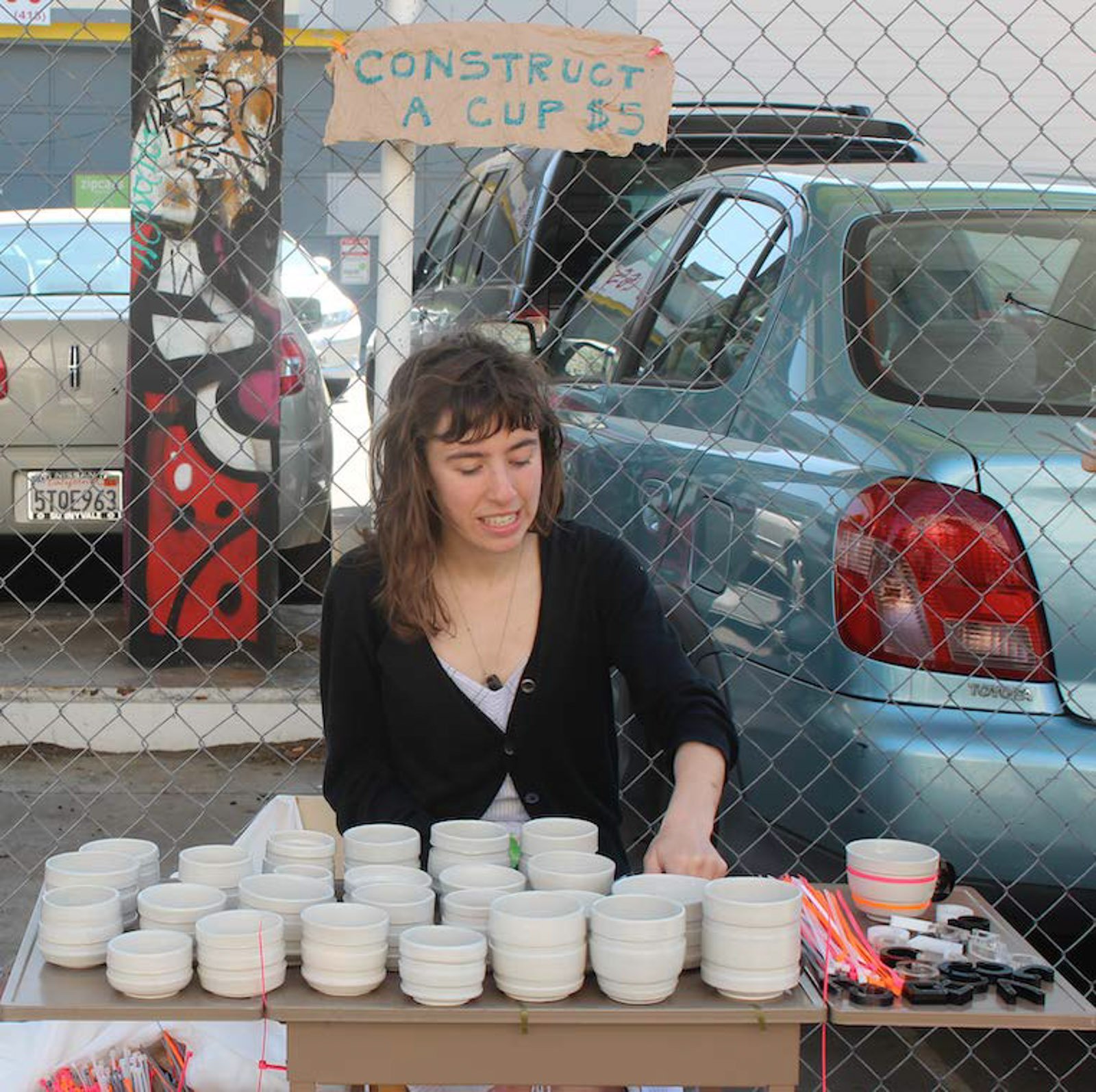 A young woman sits at a table filled with ceramic cups of various sizes and widths.