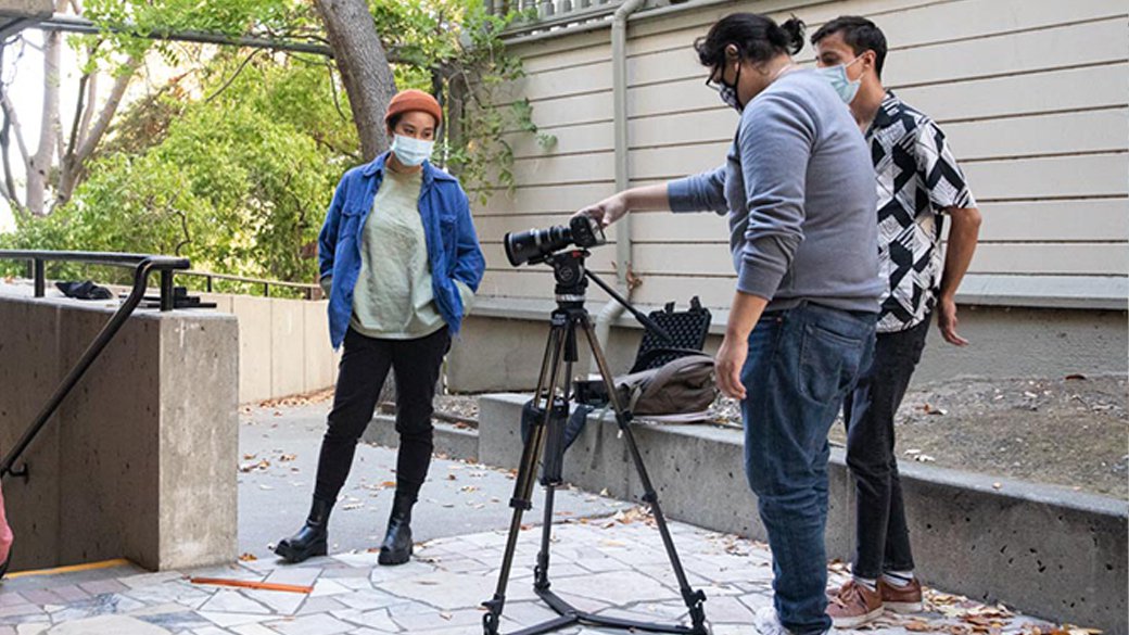 Three students prep a video shoot while one student sets up the camera.