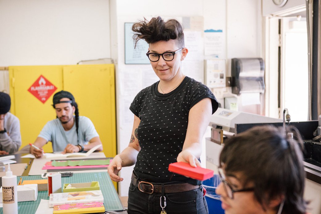 Book Arts Teacher handing something to student.