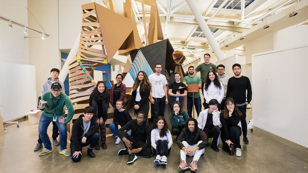 BArch Studio students pose for a photo in front of a cardboard structure.