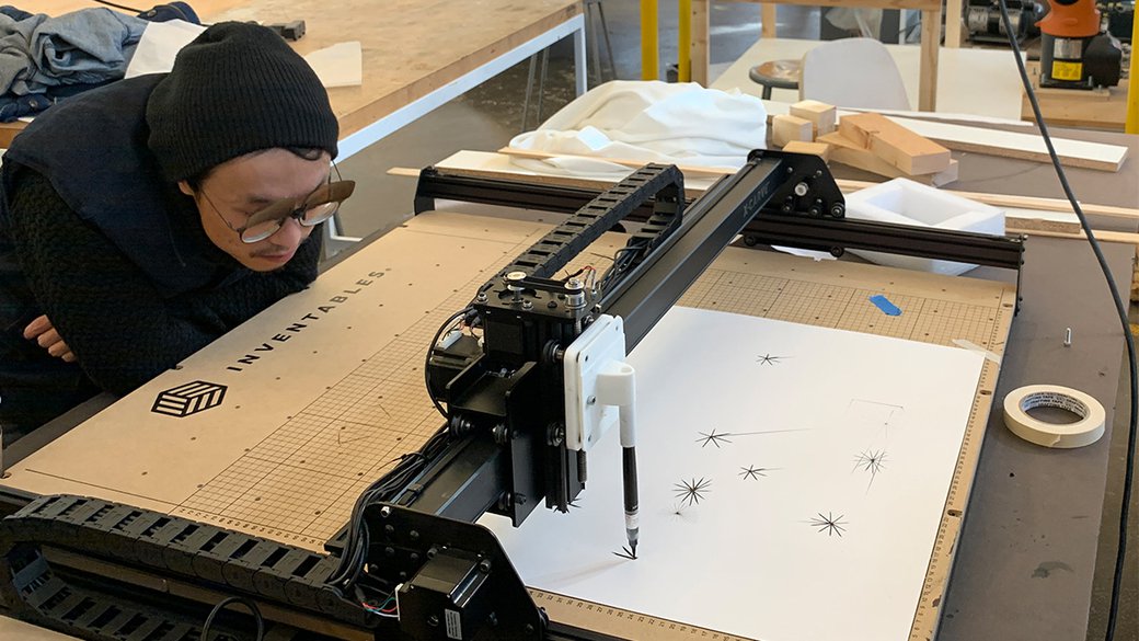An architectural student looks closely at a machine drawing on paper.