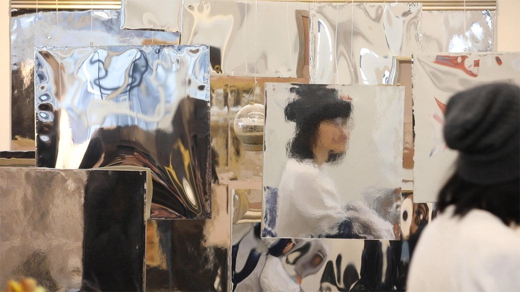 A student's face is reflected on a wall of mirrored objects.