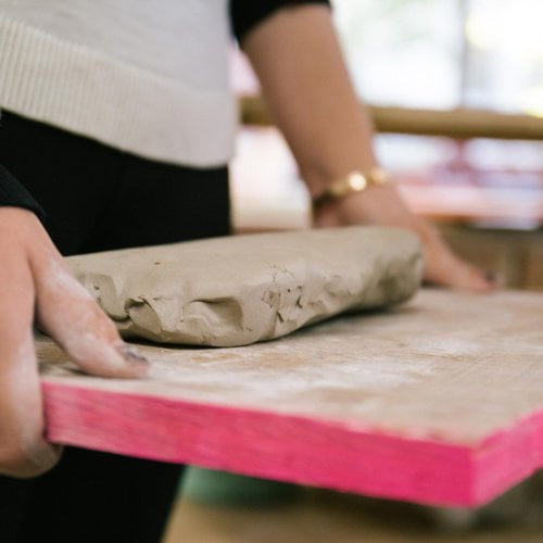 A CCA student in the Ceramics Studio with a slab of clay on a wedging board.