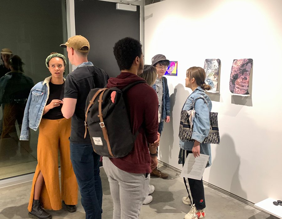 Attendees at an exhibition at the Wattis Institute for Contemporary Arts stand together viewing artwork on a wall.
