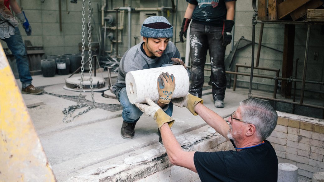 Student and faculty lift sculpture molds out of the kiln in the foundry