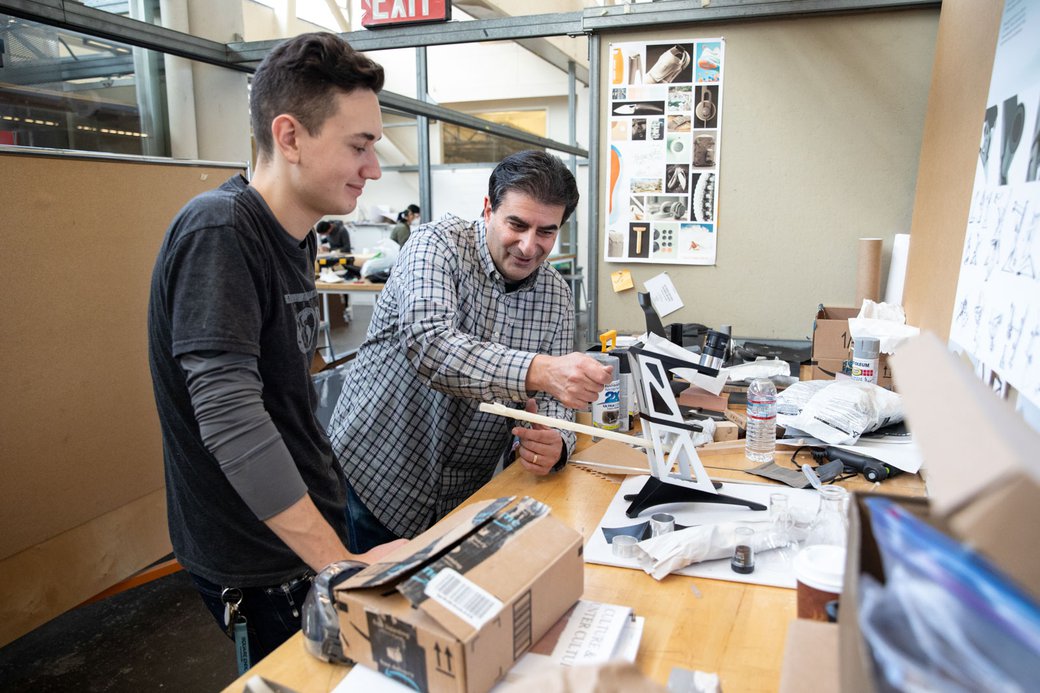 A faculty member helps an Industrial Design student with a product prototype in their personal workspace.