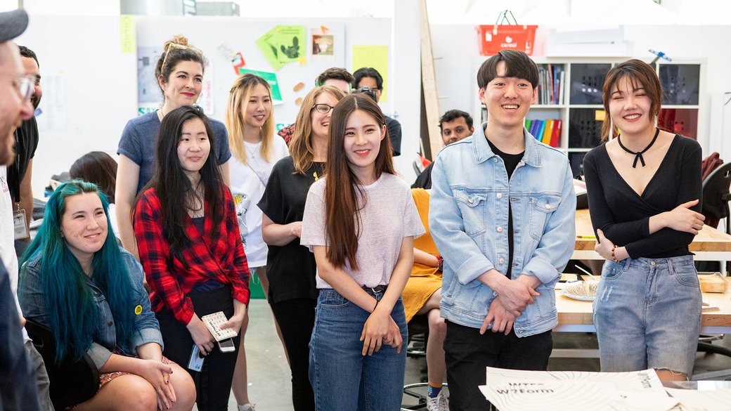 A group of smiling students stand in front of a desk posing for the photo.