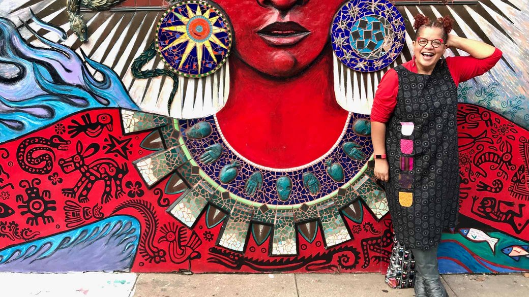 Portrait of Faith Adiele posing in front of a colorful mural.