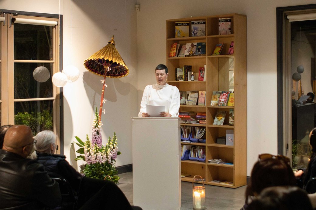 A student reads from the podium in front of a seated audience.