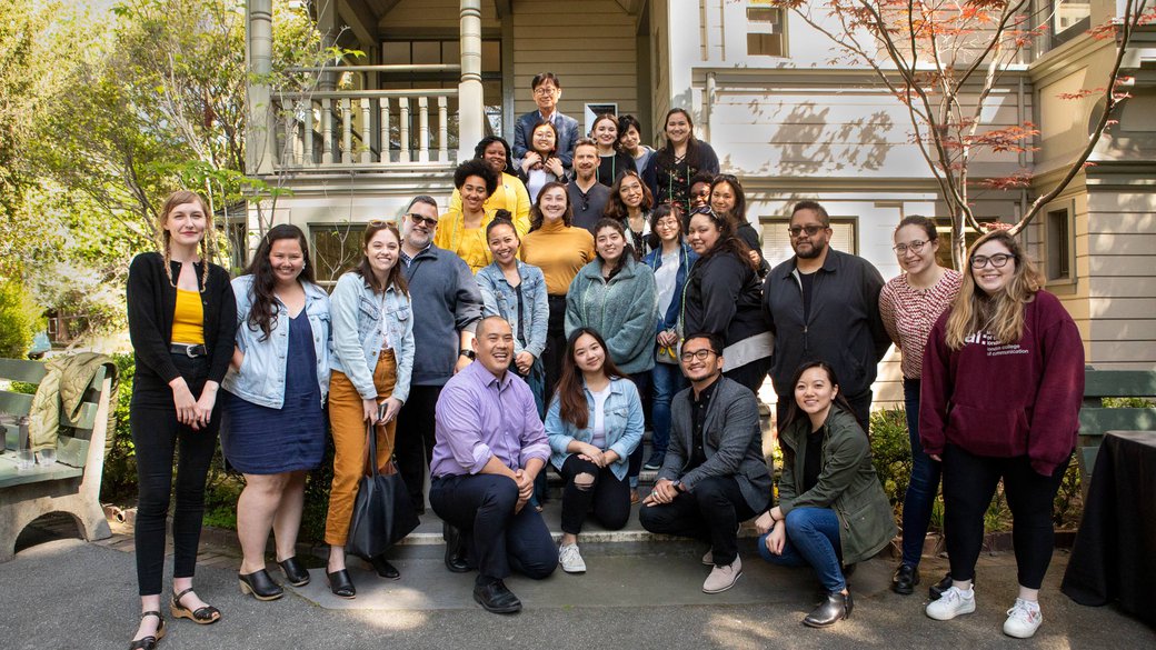 A diverse group of people pose together for a photo in front of an old house.
