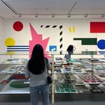 A cca study-abroad student in Seoul Korea, looking at a display case full of graphic posters in a room with similar shapes on the walls.