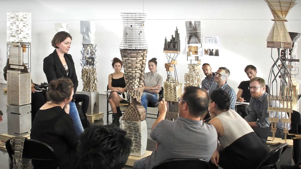 a student presenting her work to a group, surrounded by conceptual architectural models of towers
