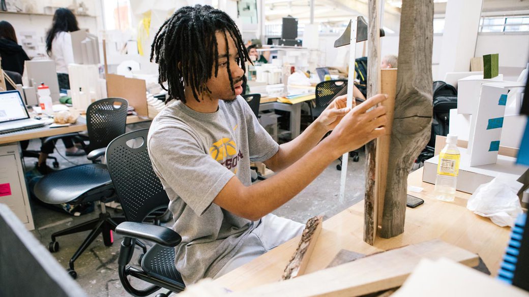 male student measuring pieces of wood for project at desk