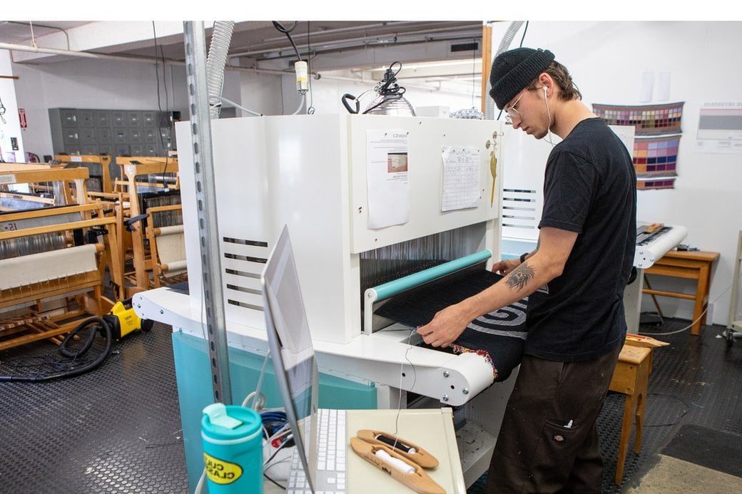A student follows a pattern while working on a weaving machine.