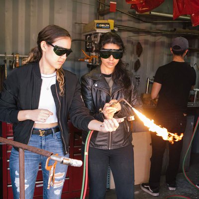 One student holds a torch, while another student ignites the flame.